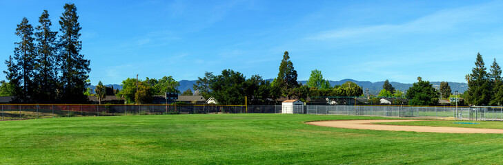 Fototapeta na wymiar Panoramic view of an empty softball, baseball field, trees and green grass in typical american residential suburban neighborhood
