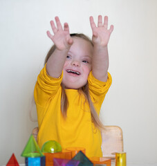 A beautiful girl with Down syndrome plays with a constructor, bright transparent figures, early...