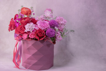 A lush bouquet of red, purple, light pink, white cute delicate small roses of different sizes, flowers in round paper box with geometric pattern. Romance.
