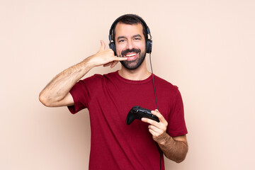 Man playing with a video game controller over isolated wall making phone gesture. Call me back sign