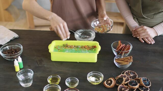 Top-view midsection PAN shot of creative women decorating and customizing handmade natural organic soap in silicon mold with dried floral petals