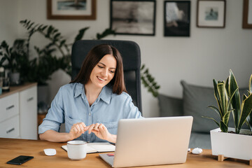 Young pretty woman talking on video call and waving hand while sitting at table in the homeoffice...