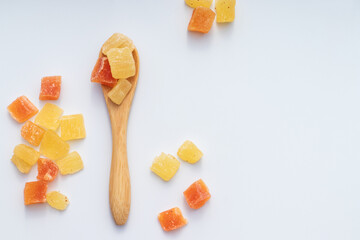 Sweet candied fruit in a wooden spoon and on a white surface.