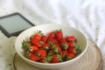 Bowl of strawberries and e-reader on a bed. Selective focus.