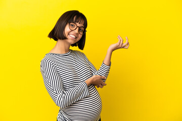 Young pregnant woman over isolated yellow background extending hands to the side for inviting to come