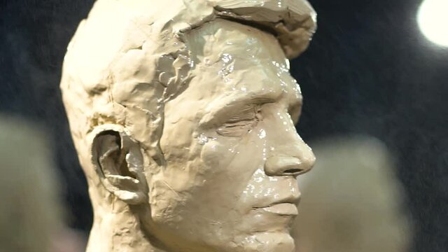 A female sculptor at work on a sculpture of a human head.