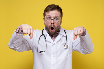 Agitated doctor in a white coat with a stethoscope around neck points down with index fingers, looks indignantly with his mouth open. 