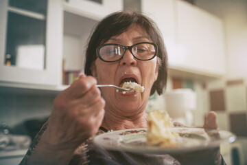 Old woman eating cake in kitchen