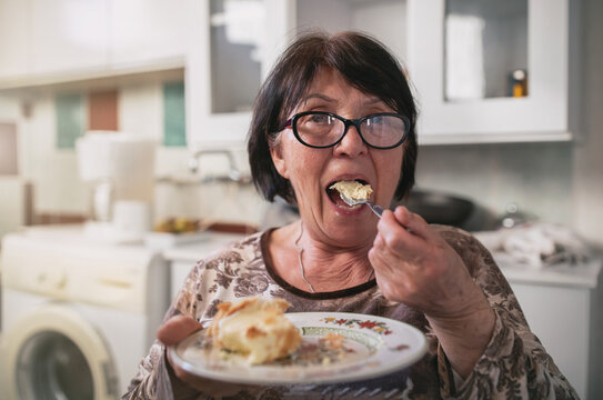 Old Woman Eating Cake In Kitchen