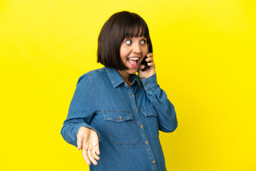 Pregnant woman using mobile phone isolated on yellow background with surprise expression while looking side