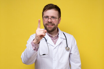 Calm, benevolent doctor raised his index finger up, he found a solution to the problem and is very happy. Yellow background.