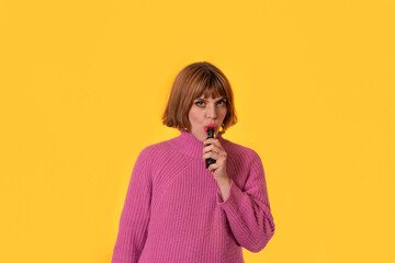 close up in front of a Yellow brackground of a sweetie girl with short Red hair, her sweater Is Pink. Shi Is smoking a elettronic sigarette