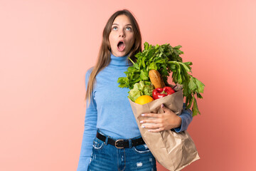 Young Lithuanian woman holding a grocery shopping bag looking up and with surprised expression