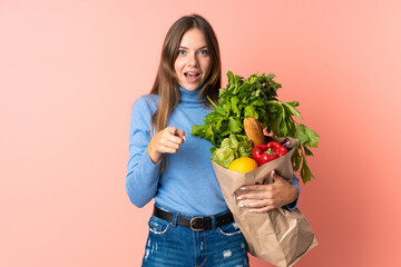 Young Lithuanian woman holding a grocery shopping bag surprised and pointing front