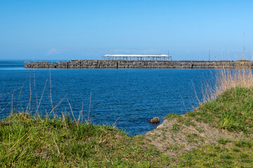 Fototapeta na wymiar Old abandoned pier seen from grassy shore