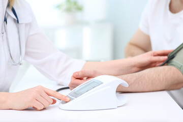 Doctor checking blood pressure of man in clinic, closeup