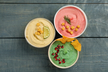 Different kinds of tasty hummus served with nachos on light blue wooden table, flat lay