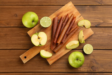 Delicious fruit leather rolls, apples and limes on wooden table, flat lay