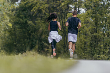 Young fit couple atheltes running on running road in a forest.