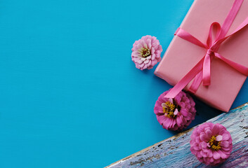 Top view of pink gift box with zinnia flowers on blue background.