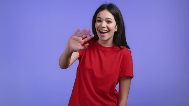 Friendly woman waving hand - hello, or goodbye, chao, adios. Parting, say bye to camera. Beautiful girl waving hand on violet studio background