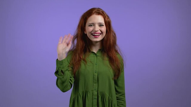 Friendly woman waving hand - hello, or goodbye, chao, adios. Parting, say bye to camera. Beautiful girl waving hand on violet studio background