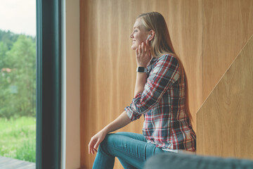 Side view of young woman listening music in earphones and sitting on steps at home