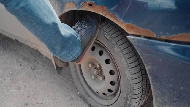 the man rests his foot on the wheel of the car and presses it to check the serviceability of the condition. The car staggers from the pressure