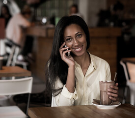 African woman smiling talking on her smart phone relaxing at the local cafe enjoying her morning coffee