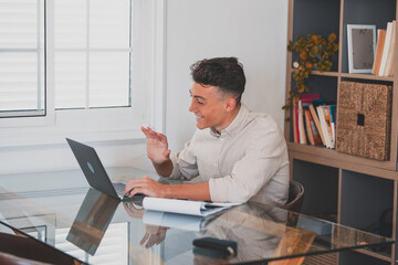 Happy young man teenager smiling and talking in video conference studying and learning online with school. Millennial doing homework at home calling .