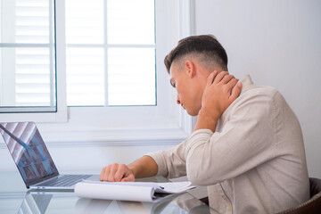 Naklejka premium Close up rear view stressed young man touching lower neck feeling discomfort, suffering from sudden pain due to sedentary lifestyle or long computer overwork in incorrect posture at home office..