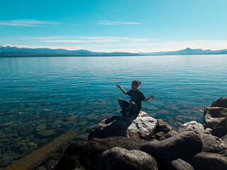 Fototapeta na wymiar hombre joven con rastas meditanto sobre rocas en el lago nahuel huapi
