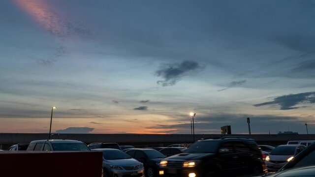 Time lapse movement real skyline with sunset and clouds in parking lot place traffic cars with light at storefront. Transportation concept.