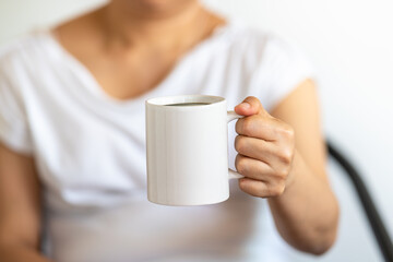 Asian woman hand holding a white cup of mug of hot black Americano coffee.