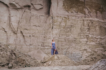 blonde hippie woman in a gray dress stands on a cave landscape