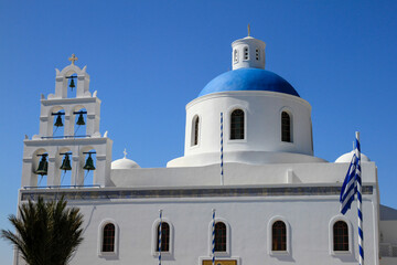 White Panagia Platsani Church with blue dome and bells against blue sky in Oia, Santorini, Greece