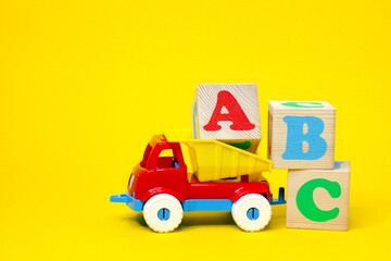 English letters ABC on wooden blocks in a toy plastic truck on a yellow background.