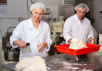Professional female baker with male assistant portioning dough with scraper and weighing pieces