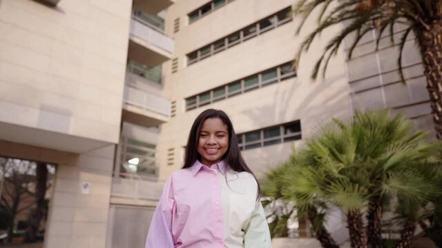 Young African American girl looking at camera outdoors, near some buildings. Shot in slow motion.