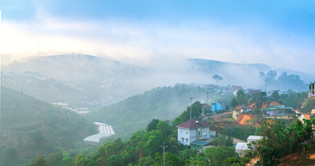 Fototapeta premium A small town under a tea hill valley in the morning with mist covering in the highlands of Da Lat, Vietnam. The place provides a great deal of tea for the whole country
