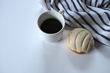 closeup of white cup of black coffee accompanied by delicious homemade Mexican shell on white cotton dishcloth with blue lines and white background