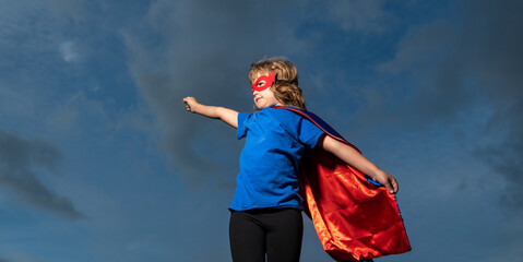 Superhero kid against dramatic blue sky background. Strong super hero boy with superpower.