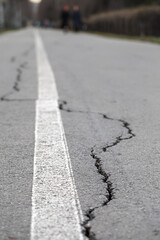 Cracks in the asphalt in the city park. Bicycle path with a white dividing strip. 