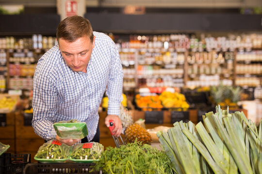 Adult man with shopping cart chooses vegetables and fruits in the store. High quality photo