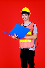 Asian engineer wearing safety suit and safety helmet standing look at camera with smiling feel happy and confident holding folder paper document on hand.Shoot in studio with red background