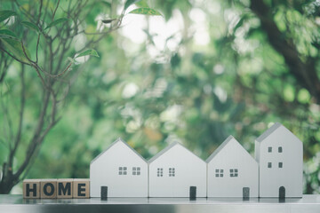 Wood cube block with word HOME with different white home against tree background.