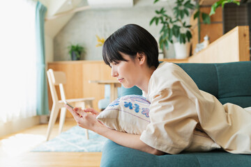 ソファに寝そべりスマートフォンを見る女性