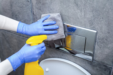 Hands in protective gloves cleaning toilet flush button