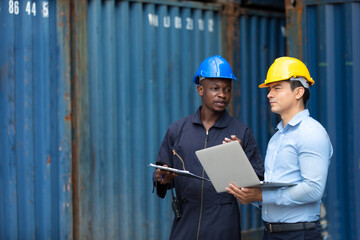 An officer from the Customs Department inspects the cargo in the container yard. Business man in hardhat helmet and African American foreman worker discuss togetherness