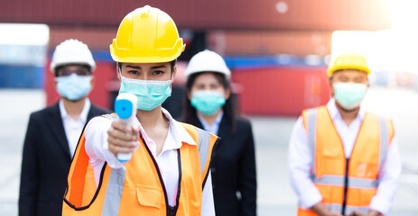 Portrait of Asian woman worker holding thermometer used to measure fever for employees at container yard. worker wearing protection face mask during coronavirus and flu outbreak.